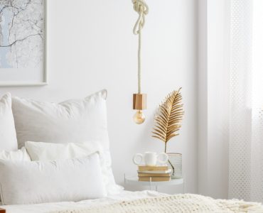 Lampe simple à ampoule suspendue par une corde au-dessus d'un lit blanc