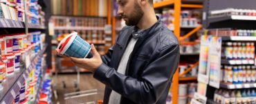 Un homme en blouson cuir noir choisissant une peinture dans une quincaillerie