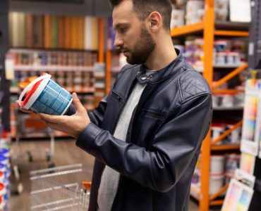 Un homme en blouson cuir noir choisissant une peinture dans une quincaillerie