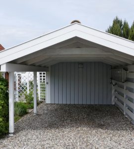 Un abri pour voiture en bois blanc sur une allée en gravier