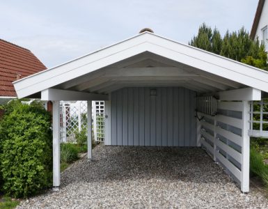 Un abri pour voiture en bois blanc sur une allée en gravier