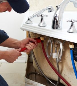 Un homme en casquette en train de fixer les tuyaux de plomberie