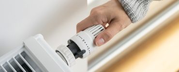 Main d'une femme réglant le thermostat du radiateur dans sa maison