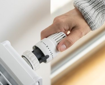 Main d'une femme réglant le thermostat du radiateur dans sa maison