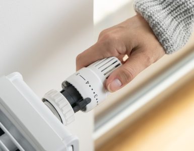 Main d'une femme réglant le thermostat du radiateur dans sa maison