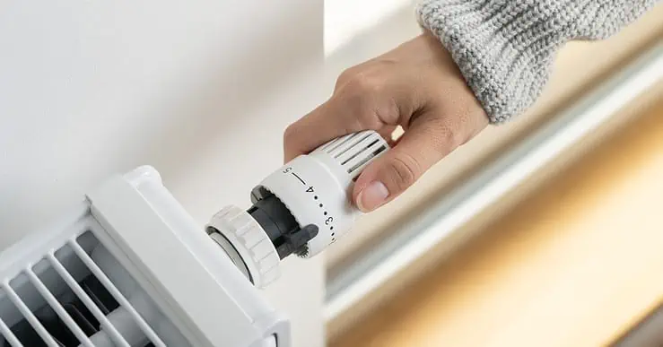 Main d'une femme réglant le thermostat du radiateur dans sa maison