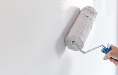 Zoom sur les mains d'un homme peignant le mur en blanc à l'aide d'un rouleau de peinture
