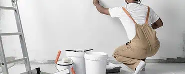 Un homme avec un casque de chantier peint un mur blanc à l’aide d’un rouleau