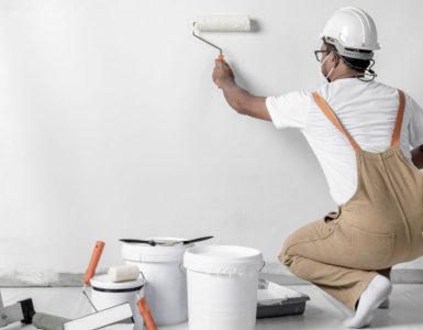 Un homme avec un casque de chantier peint un mur blanc à l’aide d’un rouleau