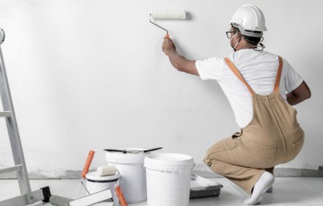 Un homme avec un casque de chantier peint un mur blanc à l’aide d’un rouleau
