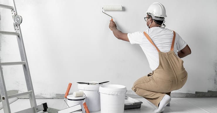 Un homme avec un casque de chantier peint un mur blanc à l’aide d’un rouleau