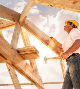 Un homme avec un marteau se tient sur une structure de toit en bois