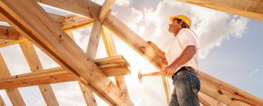 Un homme avec un marteau se tient sur une structure de toit en bois