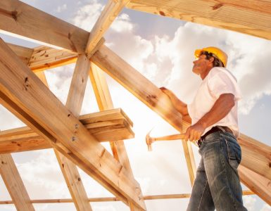 Un homme avec un marteau se tient sur une structure de toit en bois