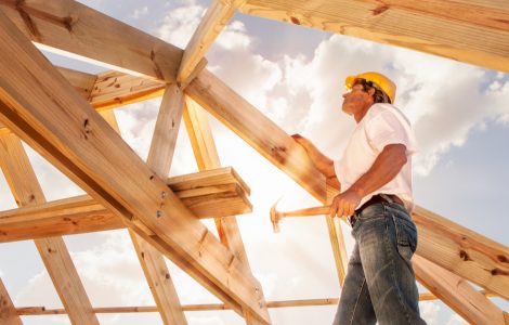 Un homme avec un marteau se tient sur une structure de toit en bois