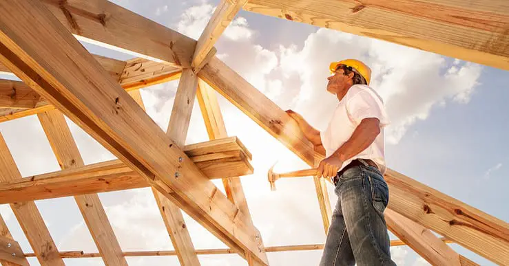 Un homme avec un marteau se tient sur une structure de toit en bois