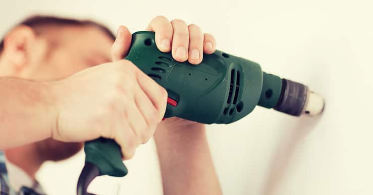 Un homme avec perceuse électrique fait un trou dans le mur