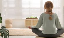Une femme en position de méditation sur un tapis rond en osier dans son salon