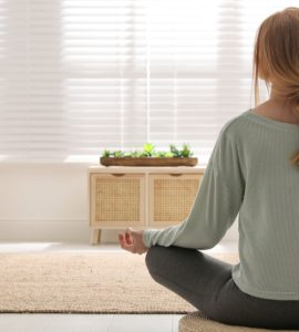 Une femme en position de méditation sur un tapis rond en osier dans son salon