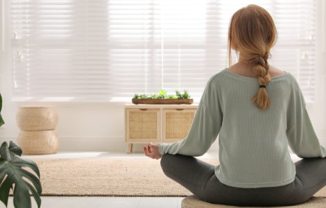 Une femme en position de méditation sur un tapis rond en osier dans son salon
