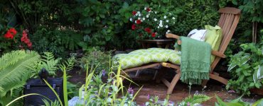 Transat en bois avec coussin et plaid dans un petit jardin