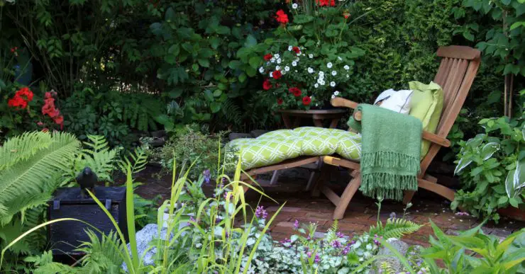 Transat en bois avec coussin et plaid dans un petit jardin