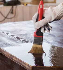 Un homme applique un vernis sur une vieille table en bois noire