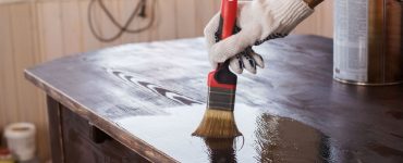 Un homme applique un vernis sur une vieille table en bois noire