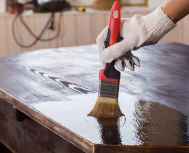 Un homme applique un vernis sur une vieille table en bois noire