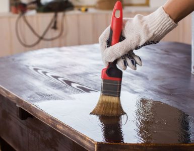 Un homme applique un vernis sur une vieille table en bois noire