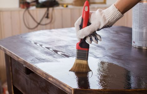 Un homme applique un vernis sur une vieille table en bois noire