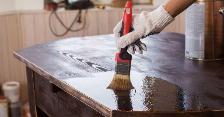 Un homme applique un vernis sur une vieille table en bois noire