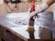 Un homme applique un vernis sur une vieille table en bois noire