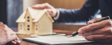 Un homme présentant un contrat avec une maquette de maison en fond