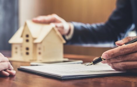 Un homme présentant un contrat avec une maquette de maison en fond