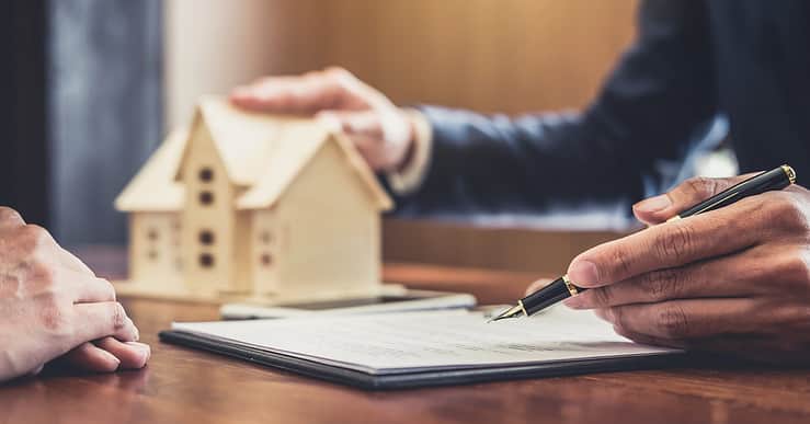 Un homme présentant un contrat avec une maquette de maison en fond