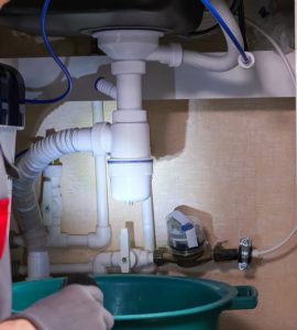 Une femme, torche à la main, regarde la fuite sous l'évier