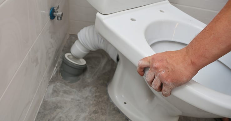 Zoom sur un homme reliant la cuvette de toilette au tuyau d'évacuation