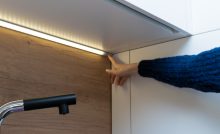 Main d'une femme montrant une bande LED allumée sous les placards cuisine