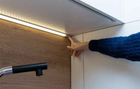 Main d'une femme montrant une bande LED allumée sous les placards cuisine