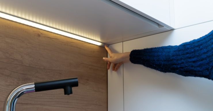 Main d'une femme montrant une bande LED allumée sous les placards cuisine