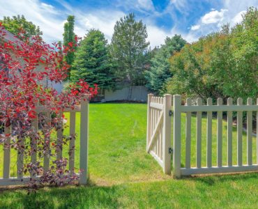 Une clôture de jardin en bois avec le portillon ouvert donnant sur la pelouse