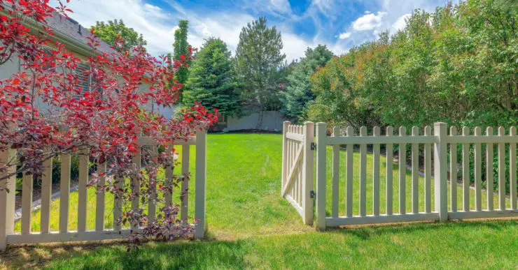 Une clôture de jardin en bois avec le portillon ouvert donnant sur la pelouse