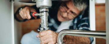 Un homme à lunettes répare une fuite d'eau sous l'évier de cuisine