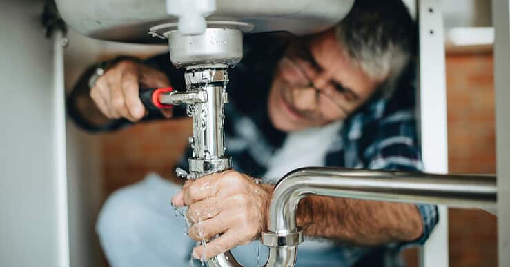 Un homme à lunettes répare une fuite d'eau sous l'évier de cuisine