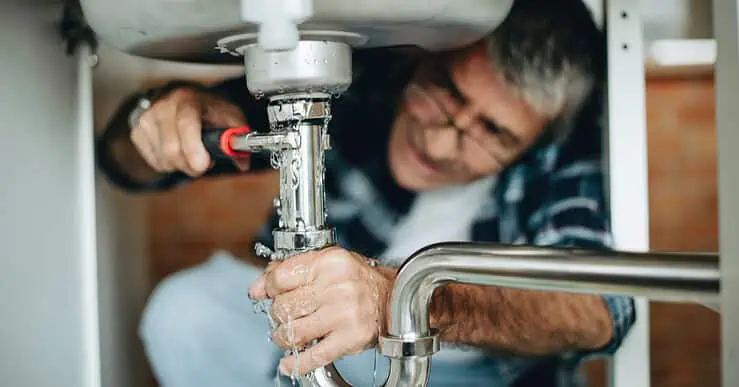 Un homme à lunettes répare une fuite d'eau sous l'évier de cuisine