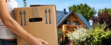 Une femme tenant un carton de déménagement avec une maison en fond