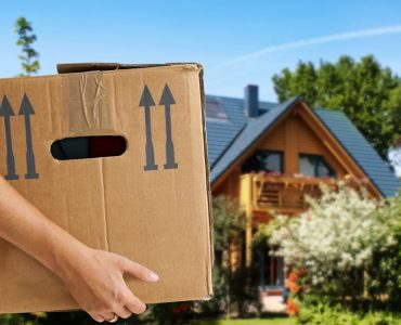 Une femme tenant un carton de déménagement avec une maison en fond
