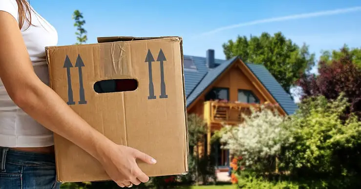 Une femme tenant un carton de déménagement avec une maison en fond