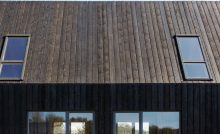 Façade d'une maison en planches de bois brûlées et des baies vitrées